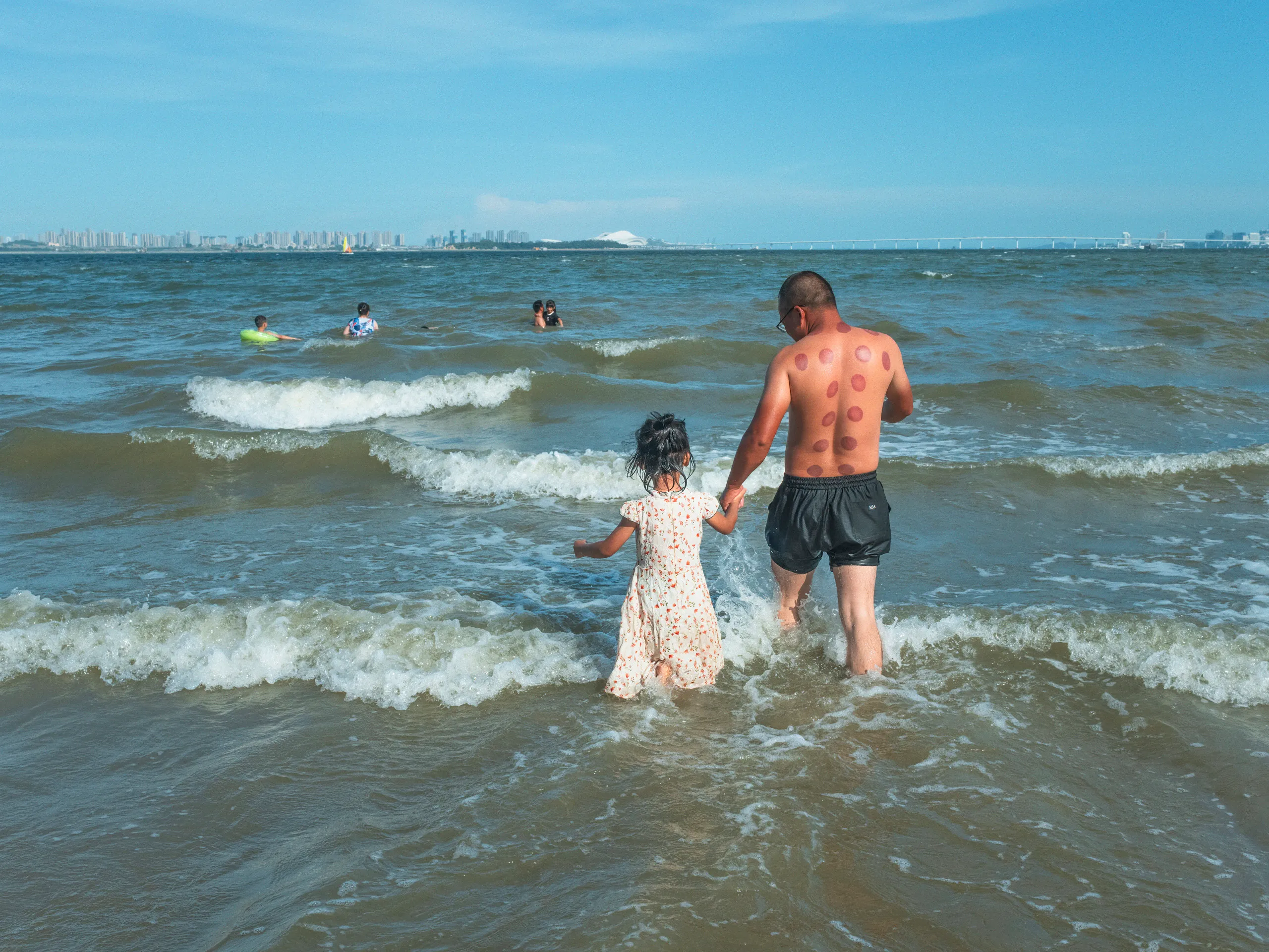 The Strip: Staying Afloat — swimming in the sea off Xiamen beach, photograph by Andras Ikladi